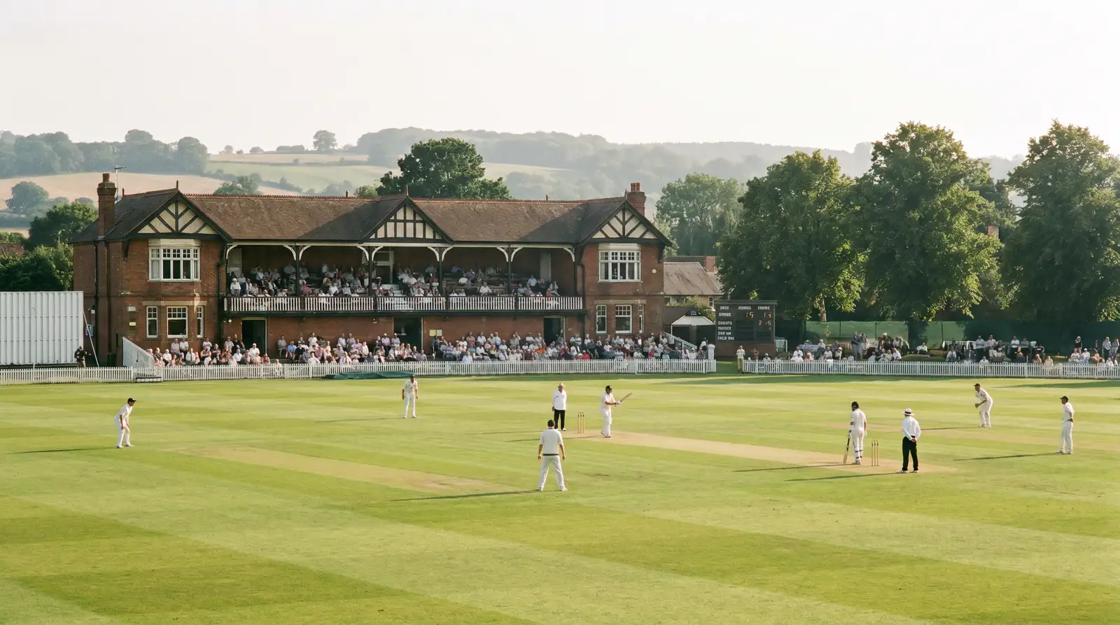 Sparsely attended county cricket ground with a small crowd in the pavilion stand