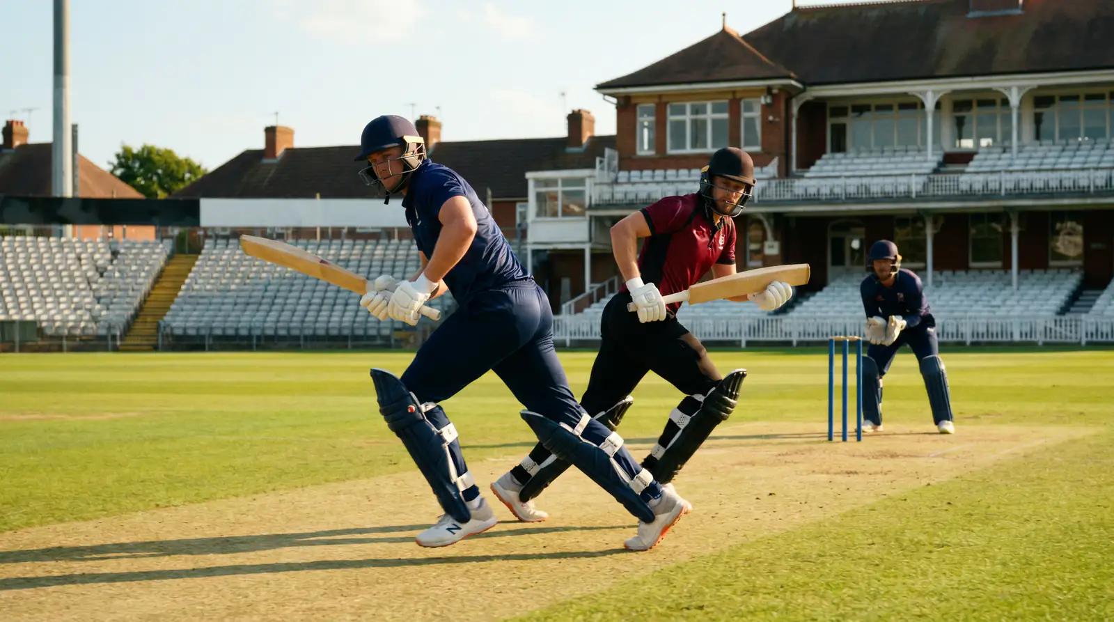 Two batters running between the wickets during a settled mid-innings partnership at an English county ground