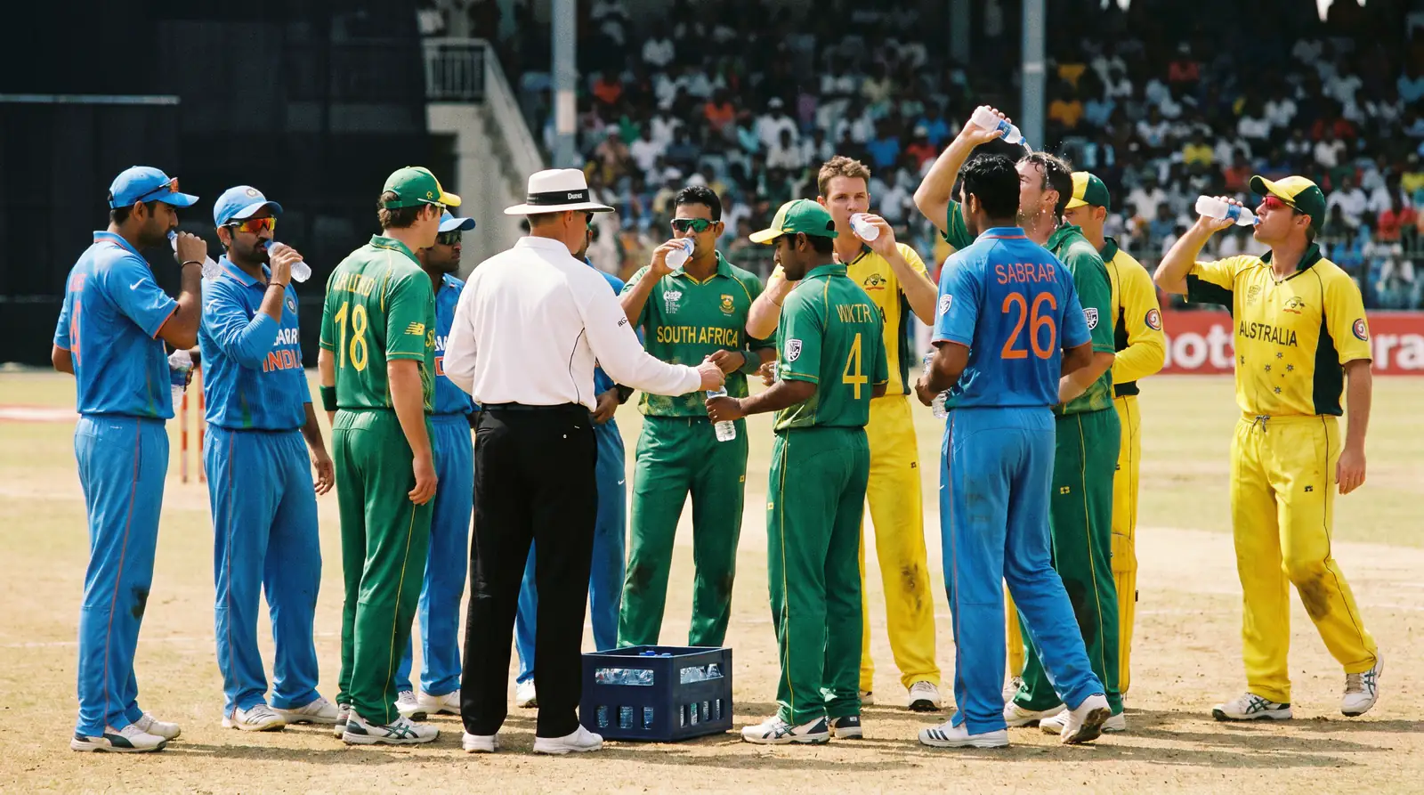 Cricket players take a drinks break as the umpires hand out water bottles mid-innings