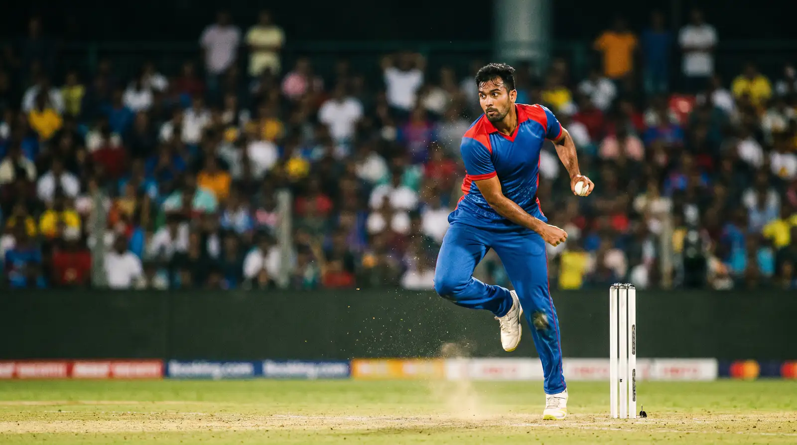 Fast bowler approaching the crease in his delivery stride during a limited-overs cricket match under floodlights