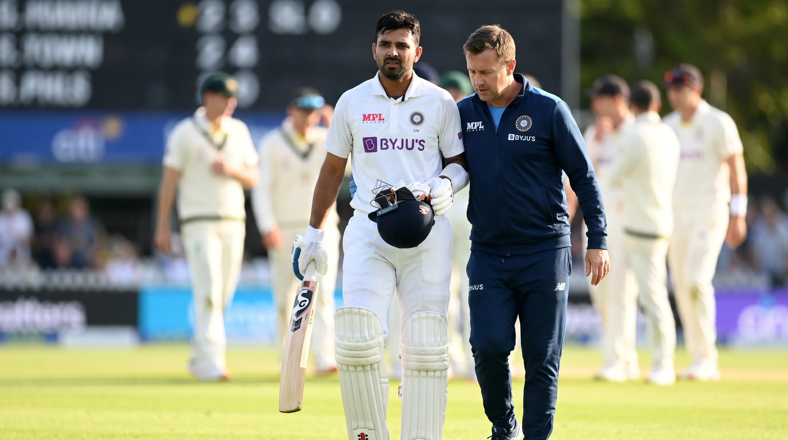 Injured cricket batter helped off the field by the physio during a match