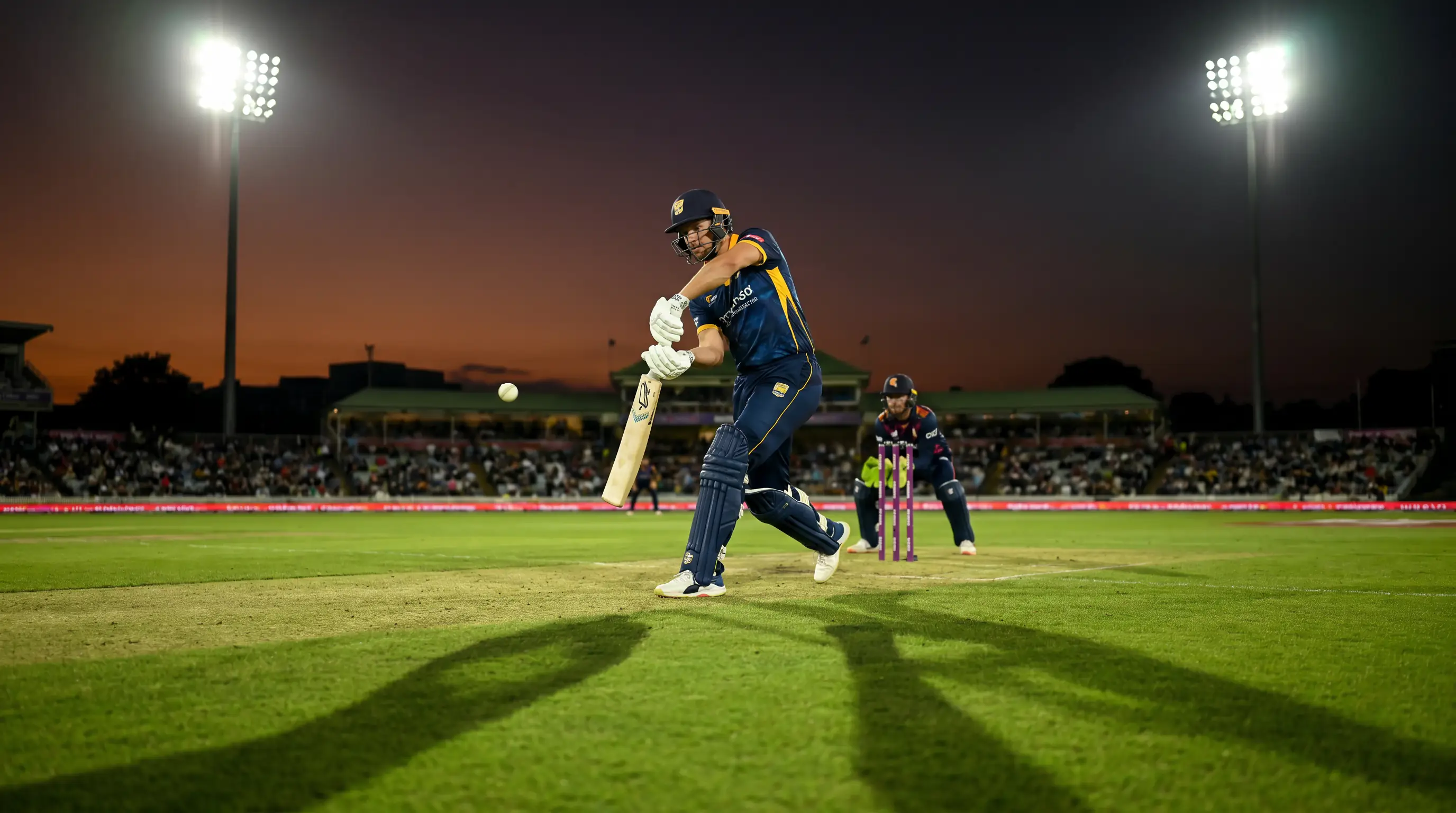 Middle order batter plays a controlled cover drive on a floodlit cricket ground