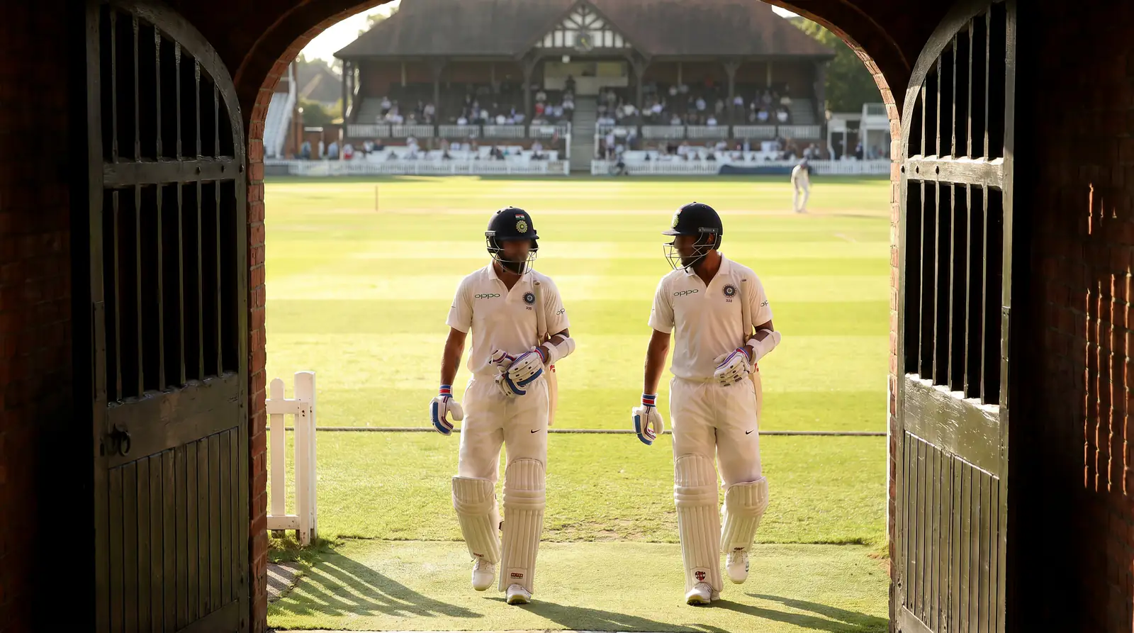 Two opening batters in pads and helmets walk out from the pavilion to start an innings